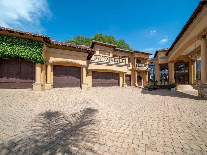 Impressive front elevation of a luxury residence featuring a spacious paved driveway, triple garage, and elegant architectural details including stone cladding and columns.