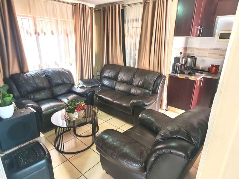 Open-plan living area featuring tiled flooring and an adjoining kitchen with built-in cabinetry and tiled backsplash.