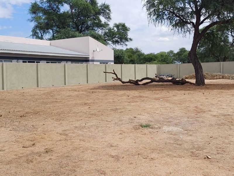 A spacious, undeveloped residential plot featuring a secure precast concrete boundary wall and a mature tree, offering a blank canvas for landscaping.