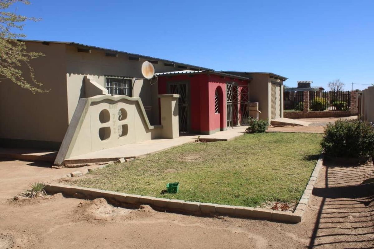 Front exterior view of a single-story house featuring a concrete boundary wall, security gates, and a small front lawn area.