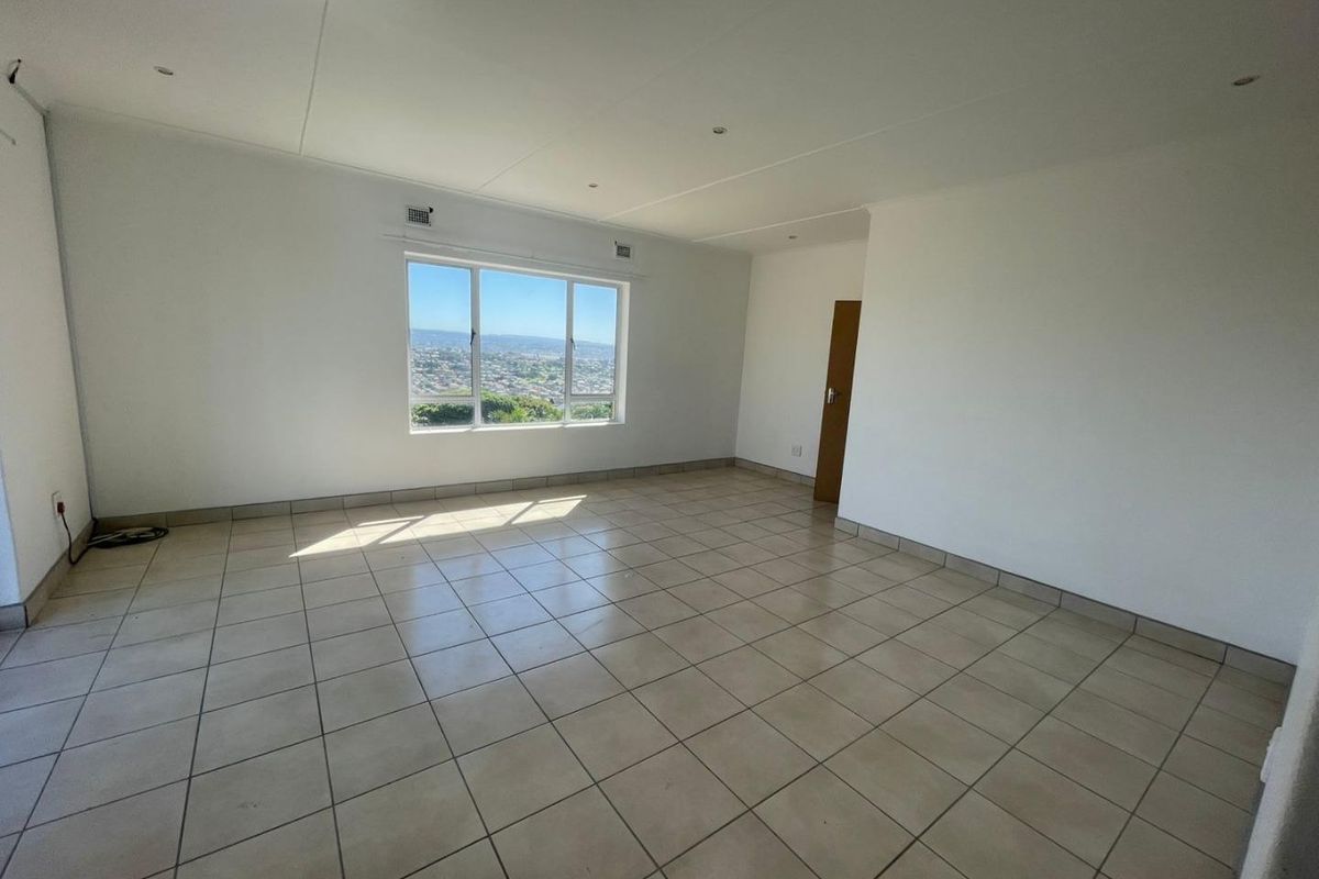 A bright, empty living room featuring neutral tiled flooring, recessed lighting, and a large window offering expansive views.