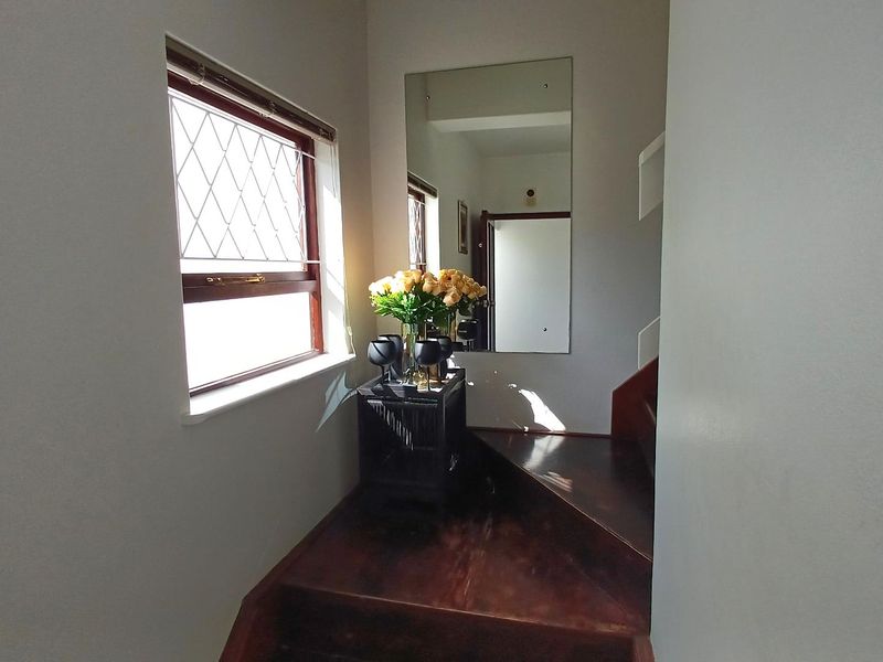 An inviting entryway featuring a timber staircase, a large wall-mounted mirror, and a window with decorative leaded glass detailing.