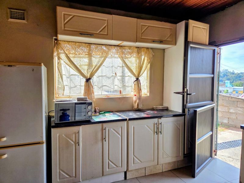 A compact kitchen featuring dated built-in cabinetry, laminate countertops, and direct access to an outdoor area through an aluminium door.