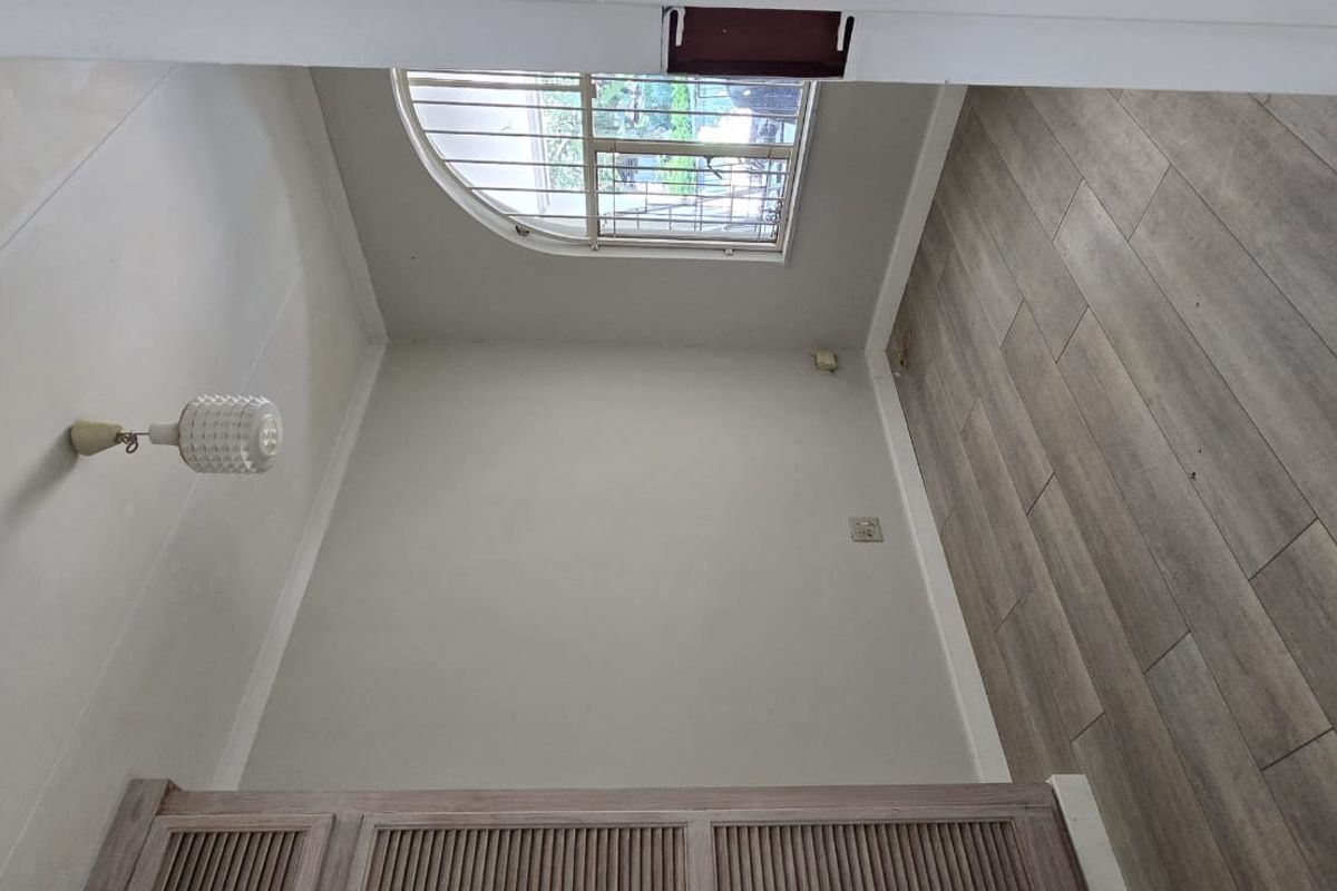 A bright, empty bedroom featuring wood-look laminate flooring, a built-in cupboard, and an arched window with security bars.