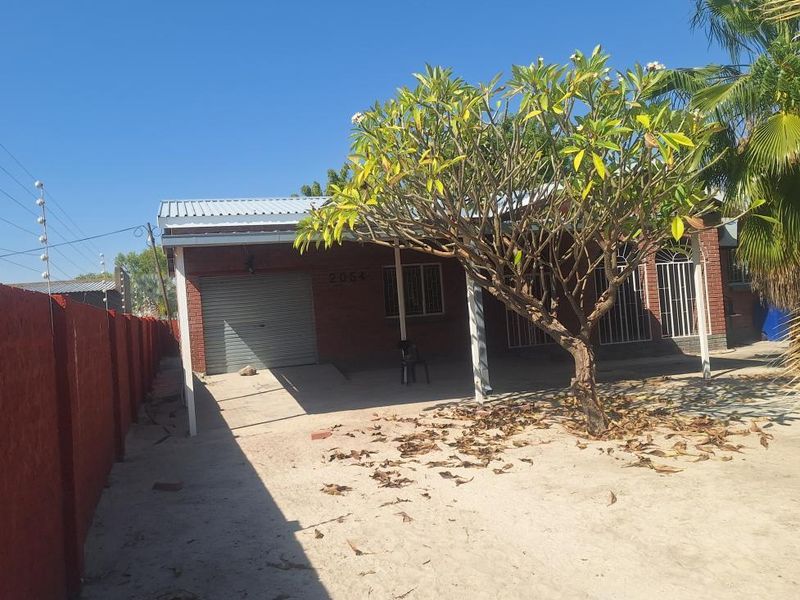 Front view of a brick house featuring a metal roller garage door, security bars on windows, and a concrete driveway.
