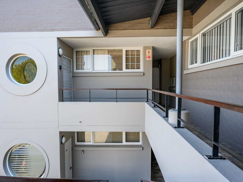 Exterior view of an apartment building featuring a multi-level walkway, circular windows, and secure metal railings.