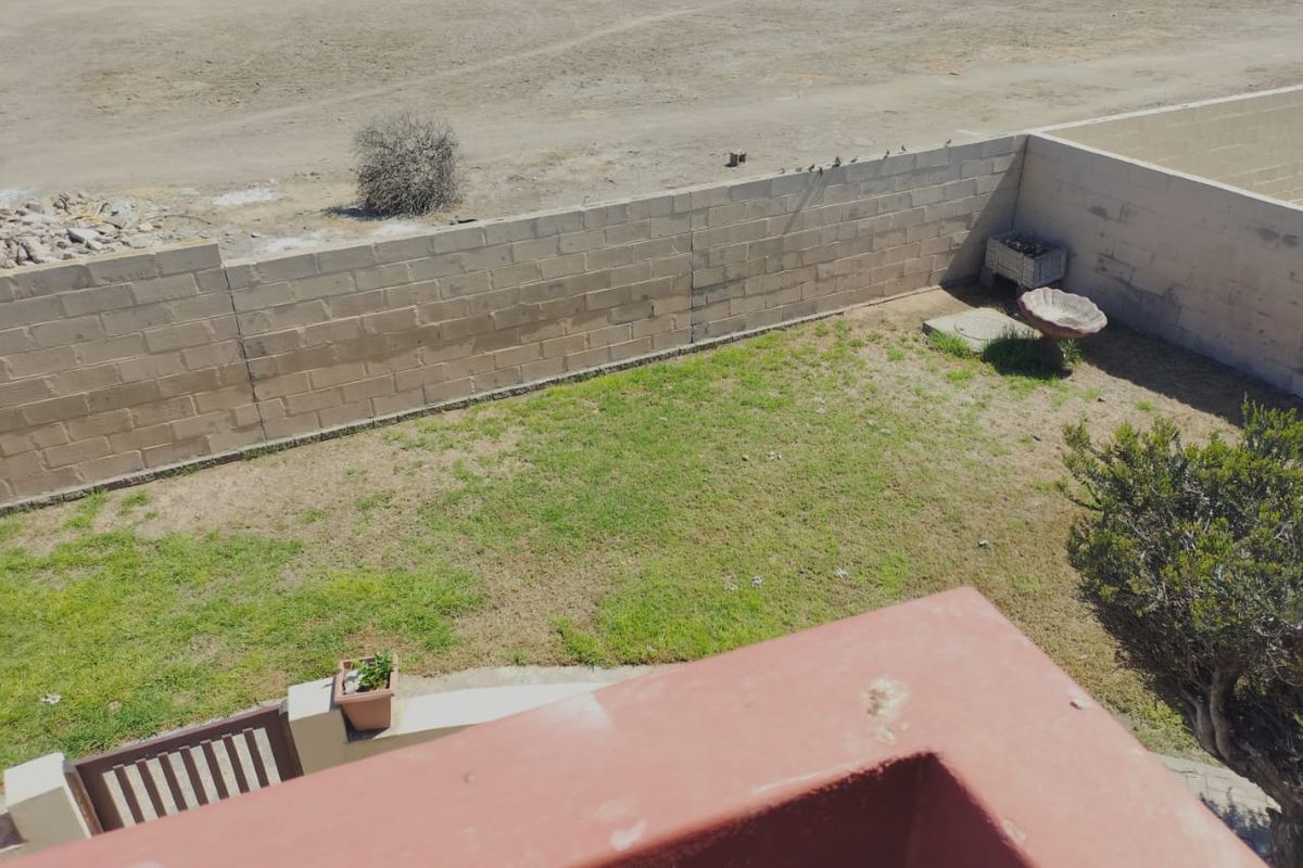 An elevated view of a rear garden featuring a lawn area enclosed by a concrete block boundary wall.
