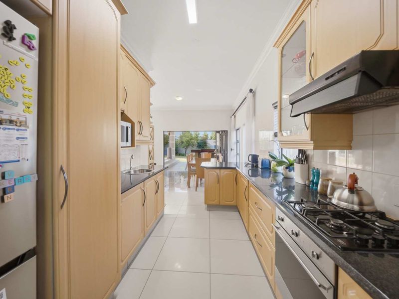 A functional galley-style kitchen featuring light wood cabinetry, granite countertops, a gas hob, and tiled flooring, leading directly into the dining area.