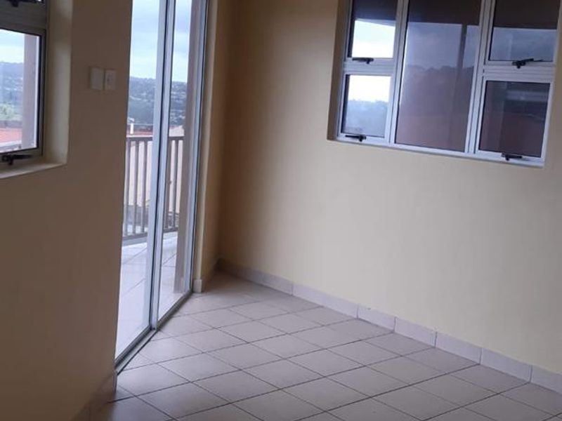 An empty living area featuring neutral tiled flooring, aluminium window frames, and a sliding door providing access to an outdoor balcony.