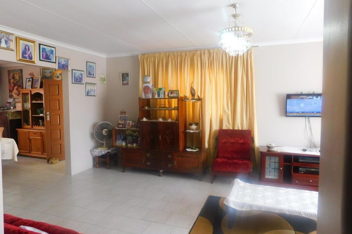 A spacious living room featuring tiled flooring, a decorative crystal chandelier, and coved ceiling details, offering a functional and well-lit living space.