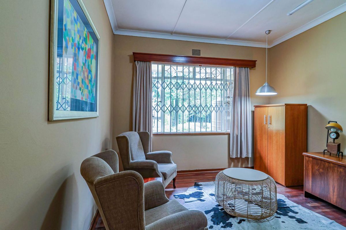 A cozy living room featuring hardwood flooring, a large window with security bars, and a pendant light fixture.