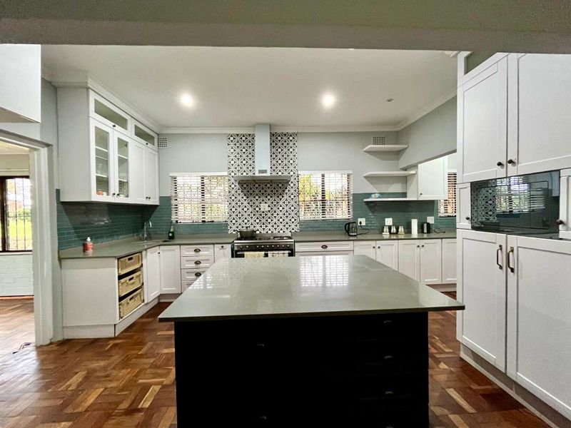 Modern kitchen featuring a central island, quartz countertops, shaker-style cabinetry, patterned tile backsplash, and warm parquet flooring with integrated appliances.