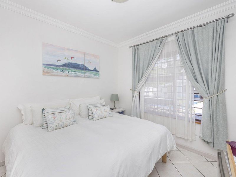 A bright and well-maintained bedroom featuring tiled flooring, crown molding, and large windows with installed curtain rods.