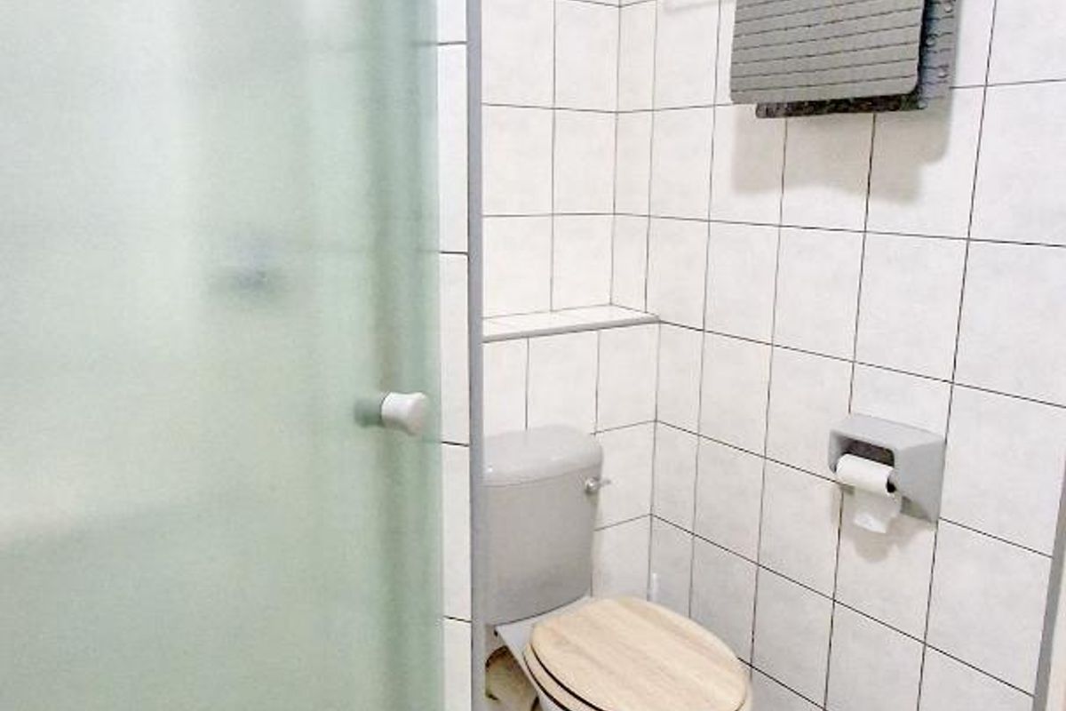 A functional bathroom featuring a glass-enclosed shower, tiled walls, and standard sanitary fixtures.