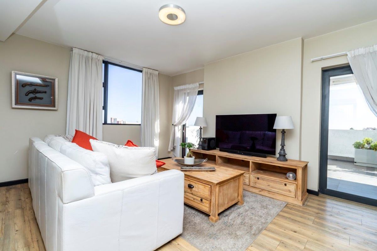 A bright living room featuring wood-look flooring, large windows, and direct access to an outdoor balcony area.