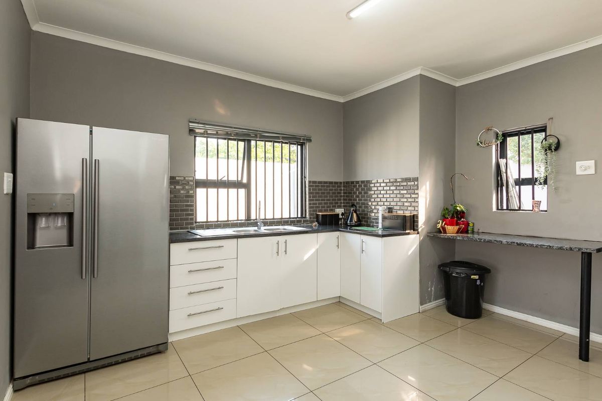 Modern kitchen featuring white cabinetry, dark subway tile backsplash, granite-style countertops, tiled flooring, and security bars on windows.