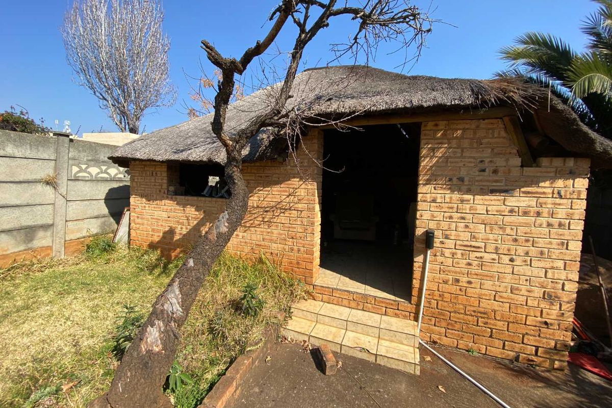 Rear view of a face brick outbuilding featuring a traditional thatch roof and a tiled entrance step, set within a garden area.