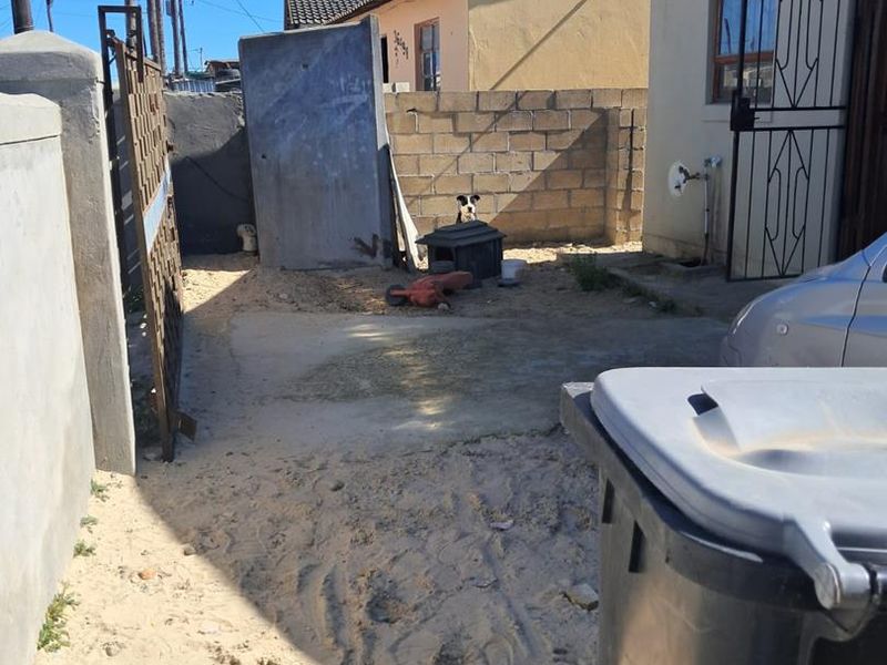 Rear exterior area featuring a concrete block boundary wall, security gate, and paved section, currently requiring landscaping and surface improvements.