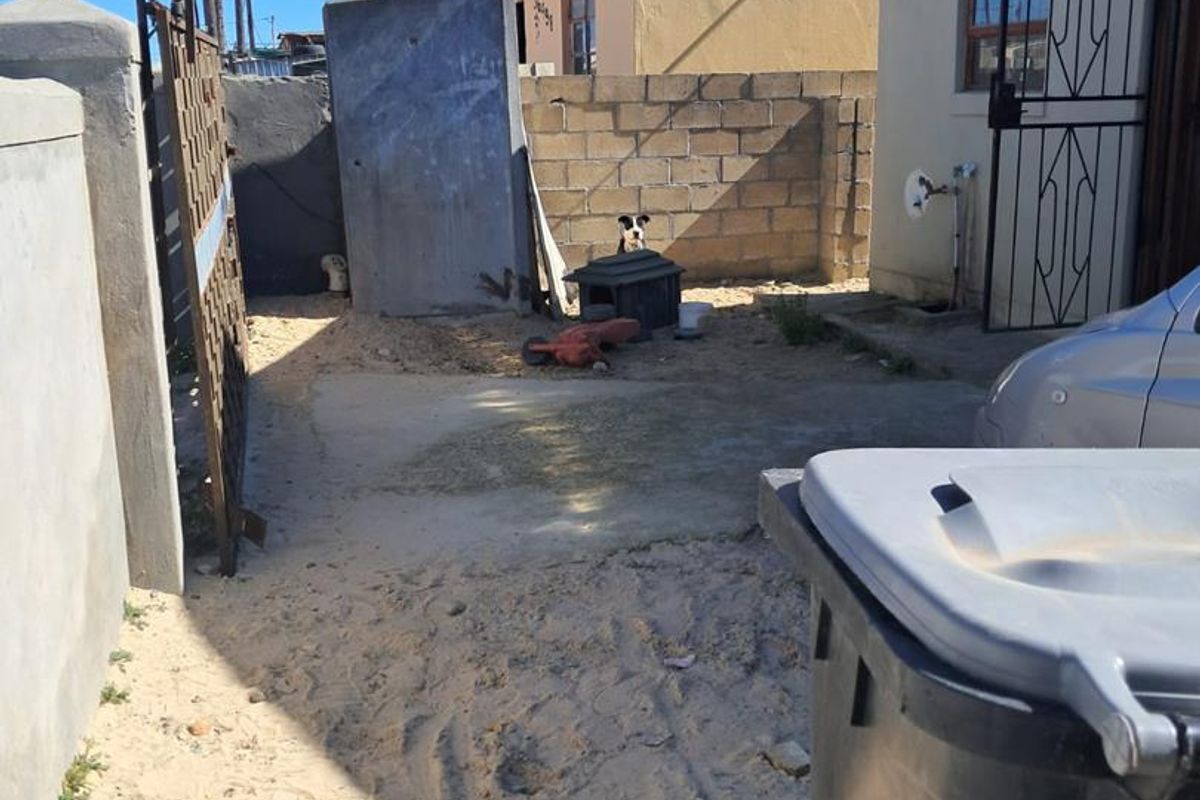Rear exterior area featuring a concrete block boundary wall, security gate, and paved section, currently requiring landscaping and surface improvements.