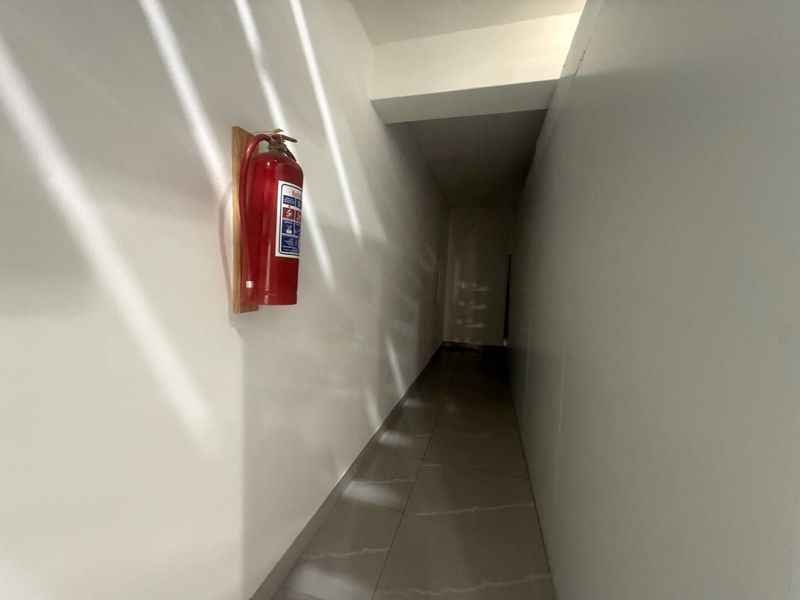 A clean, minimalist hallway featuring tiled flooring and a wall-mounted fire extinguisher.