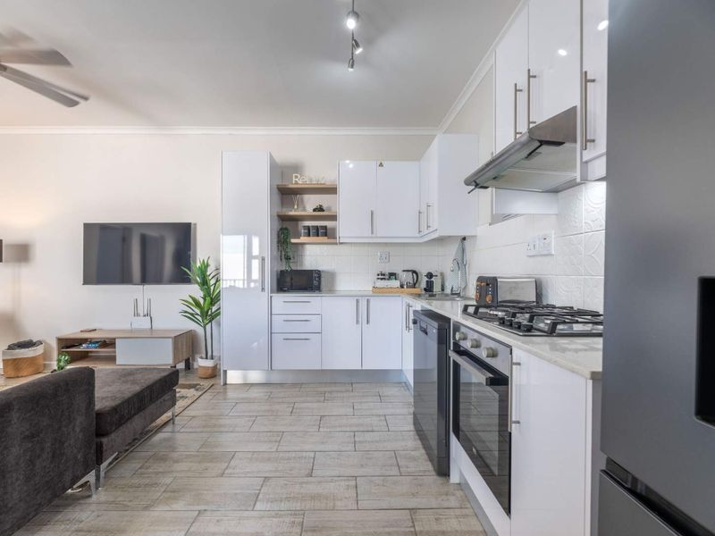 Modern open-plan living area featuring a well-equipped kitchen with white cabinetry, gas hob, oven, and tiled flooring throughout.