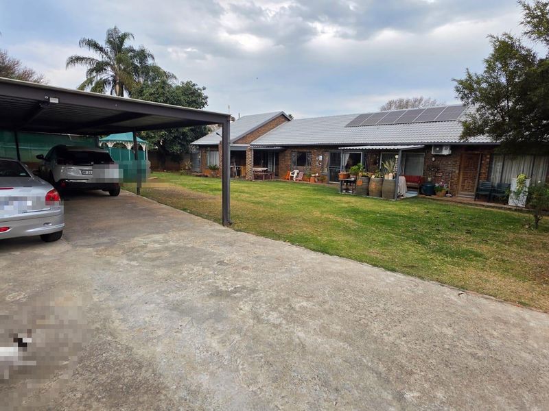 Rear view of the property featuring a spacious lawn, brick facade, tiled roof with solar panels, and a covered carport area.