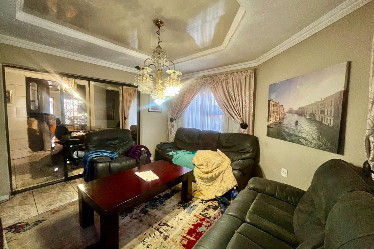 A living room featuring a tray ceiling with a decorative chandelier, tiled flooring, and a large mirrored wall panel.