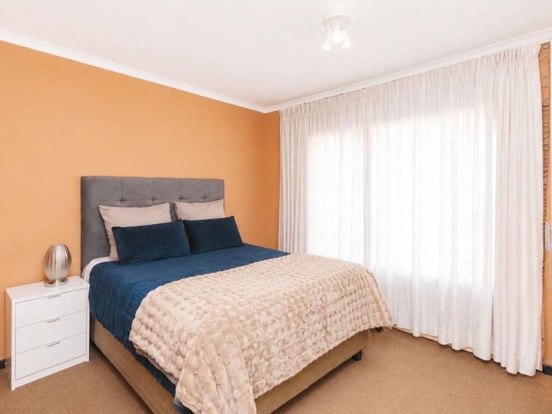 A bedroom featuring carpeted flooring, neutral wall paint, and large windows with installed curtain tracks.