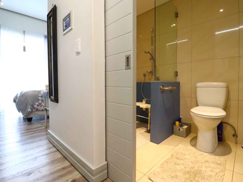 A modern bathroom featuring a sliding door, glass-enclosed shower, and neutral wall tiling, adjacent to a bedroom area.