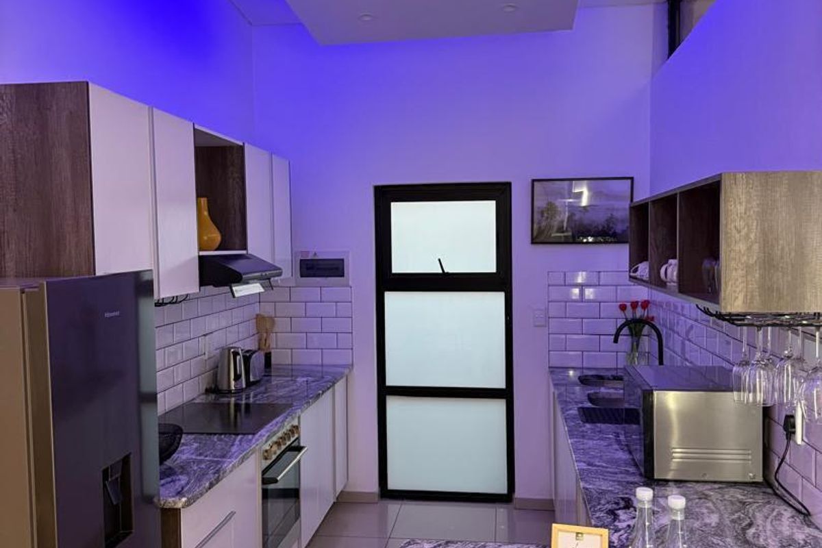 Modern kitchen featuring stone countertops, subway tile backsplash, built-in oven, hob, and integrated lighting with a contemporary glass panel door.