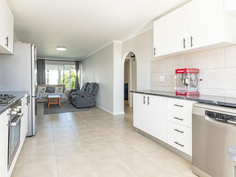 Open-plan kitchen and living area featuring modern white cabinetry, stone countertops, tiled flooring, and direct access to the outdoor space through sliding doors.