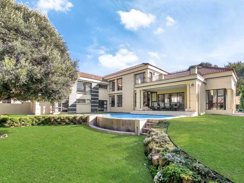Spacious rear exterior view featuring a well-maintained garden, a raised swimming pool, and a large double-story residence with a balcony and patio area.