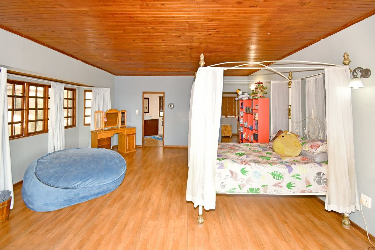 Spacious bedroom featuring timber ceiling, laminate flooring, and direct access to an en-suite bathroom.