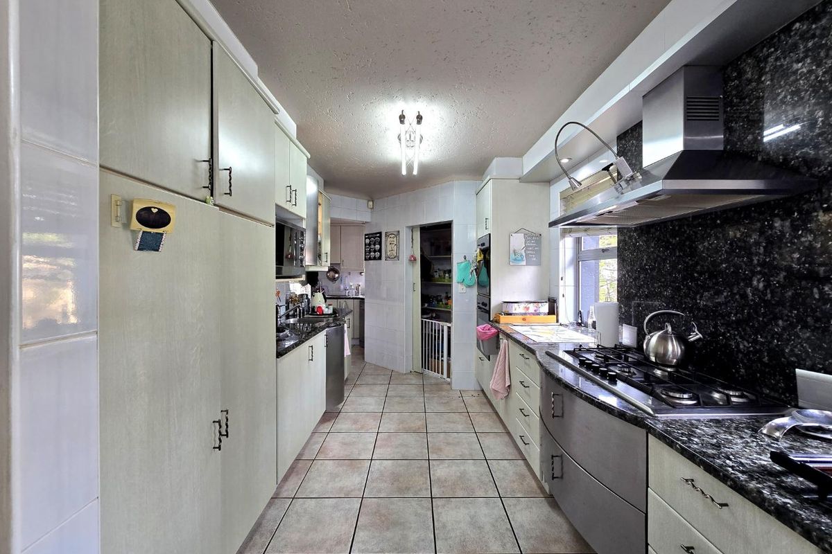 A functional galley-style kitchen featuring granite countertops, built-in gas hob, stainless steel extractor fan, and ample cabinetry storage.