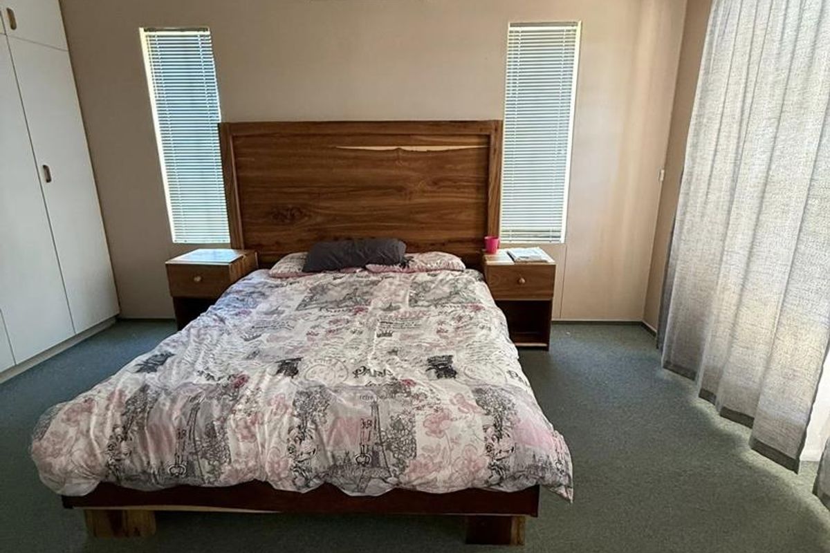 A well-lit bedroom featuring built-in wardrobes, a wall-mounted air conditioning unit, and dual windows with fitted blinds.