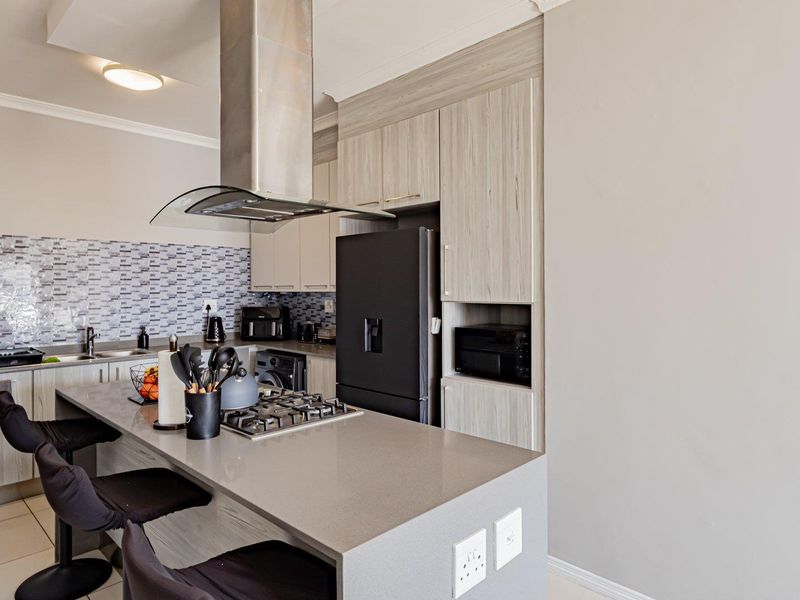 Modern kitchen featuring light wood-grain cabinetry, stone countertops, a central island with a gas hob, and a stylish mosaic tile backsplash.