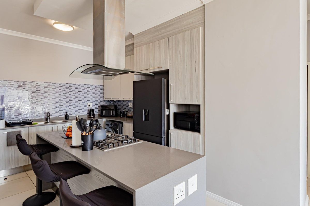 Modern kitchen featuring light wood-grain cabinetry, stone countertops, a central island with a gas hob, and a stylish mosaic tile backsplash.