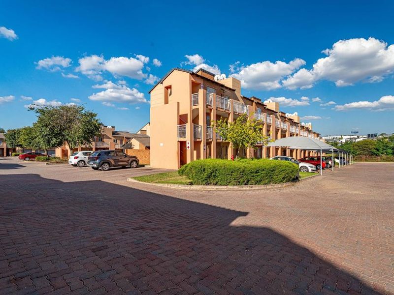 Exterior view of a multi-story apartment complex featuring paved parking areas, covered carports, and private balconies for each unit.