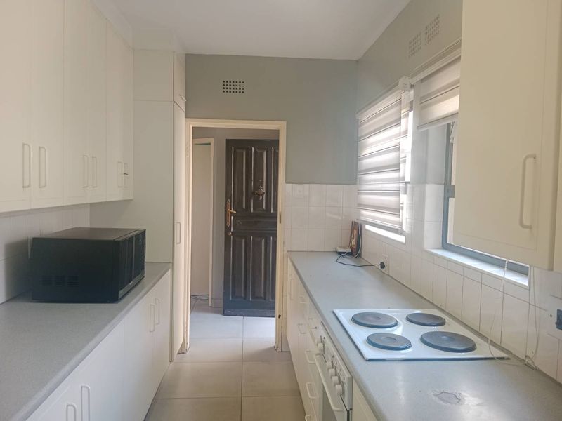 A functional kitchen featuring white cabinetry, a built-in electric hob and oven, tiled backsplash, and neutral tiled flooring.