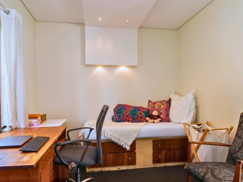 A compact bedroom featuring a built-in bed base with integrated storage drawers, recessed ceiling lighting, and a large window with timber frames.