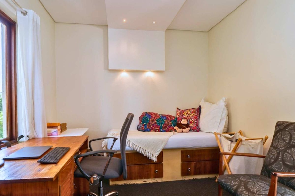 A compact bedroom featuring a built-in bed base with integrated storage drawers, recessed ceiling lighting, and a large window with timber frames.