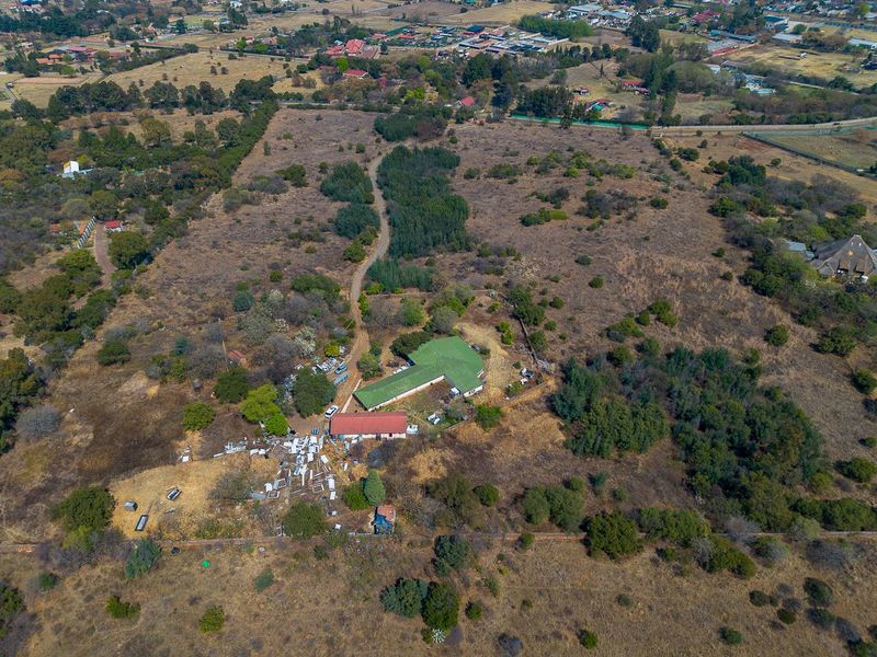 Aerial view of a large residential vacant land plot featuring existing structures, natural vegetation, and a dirt access road.