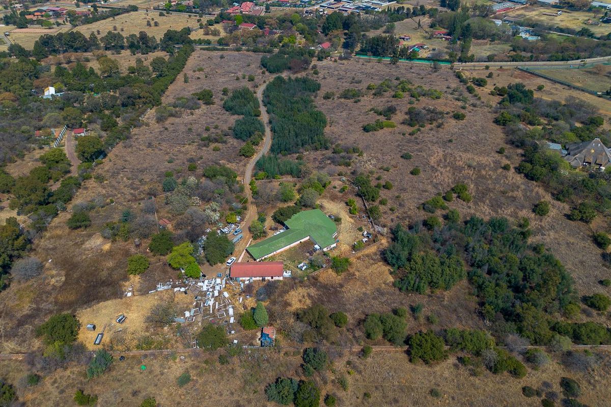 Aerial view of a large residential vacant land plot featuring existing structures, natural vegetation, and a dirt access road.