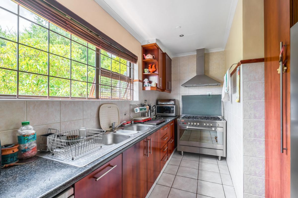 A functional galley-style kitchen featuring dark wood cabinetry, granite countertops, a stainless steel gas stove with extractor fan, and tiled flooring.