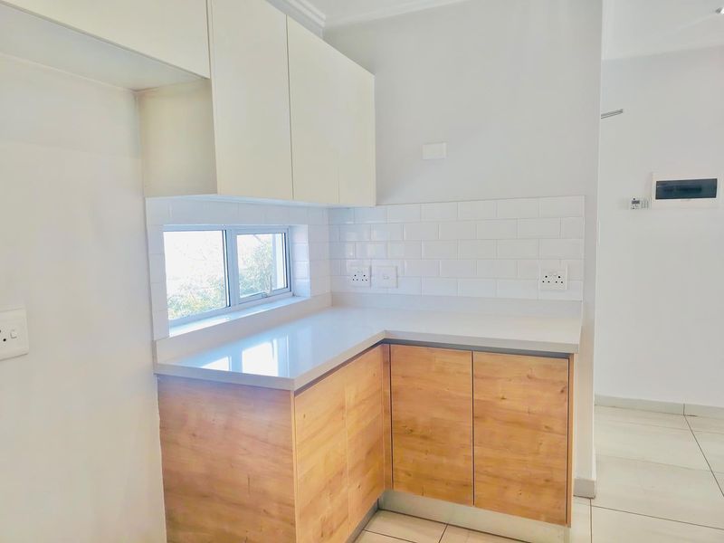 A modern, clean kitchen area featuring light wood-finish lower cabinetry, white upper cabinets, stone countertops, and a classic white subway tile backsplash.