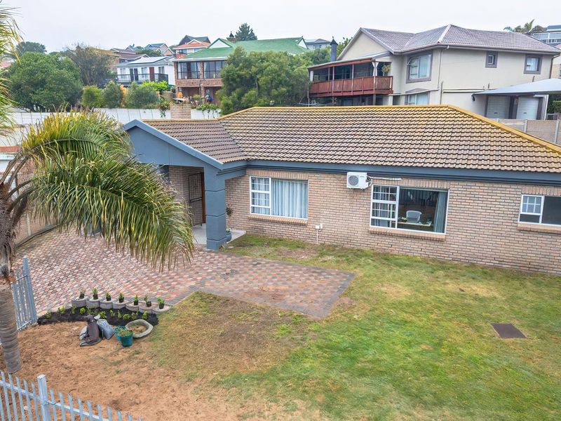 An elevated view of the front exterior featuring a brick facade, tiled roof, paved driveway, and a lawn area.
