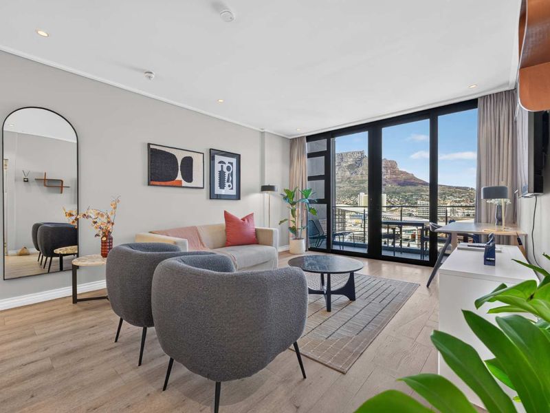 Modern living room featuring light laminate flooring, recessed lighting, and large sliding glass doors opening to a balcony with mountain views.