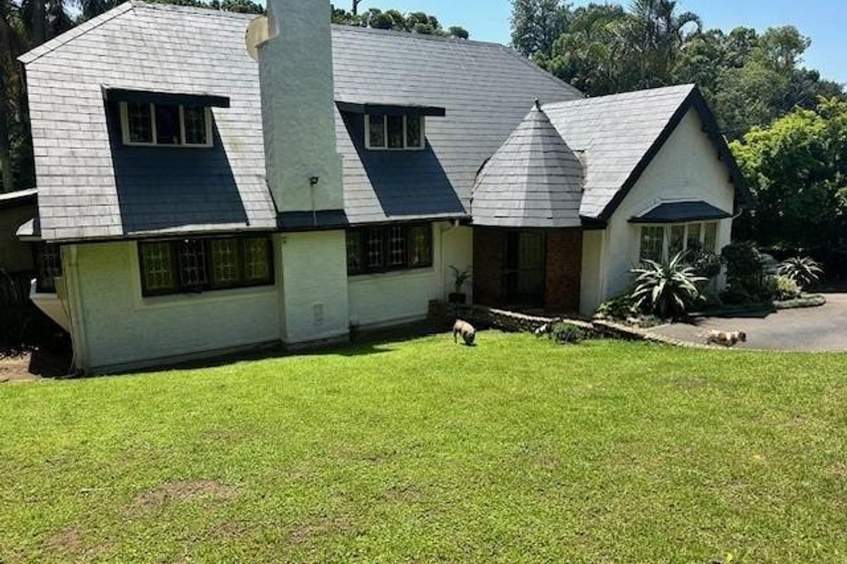 Rear view of a characterful home featuring a slate roof, prominent chimney, and a unique turret architectural detail set against a large lawn.