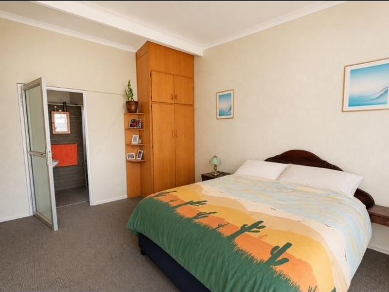 A bedroom featuring built-in wooden cabinetry and direct access to an en-suite bathroom, offering a functional layout with neutral wall finishes.