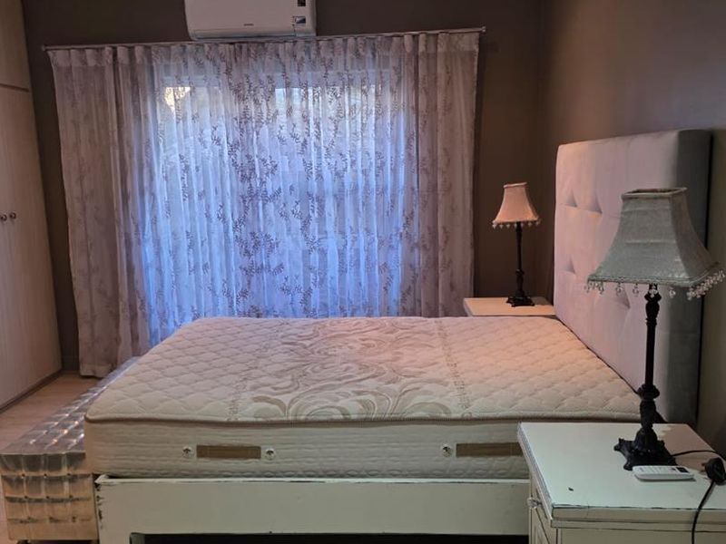 A well-proportioned bedroom featuring laminate flooring, built-in wardrobe storage, and a wall-mounted air conditioning unit for climate control.